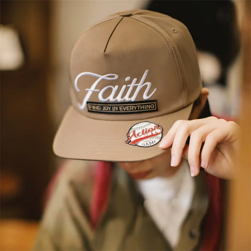 Beige cap with 'Faith' and 'Action' logos, worn by a person.
